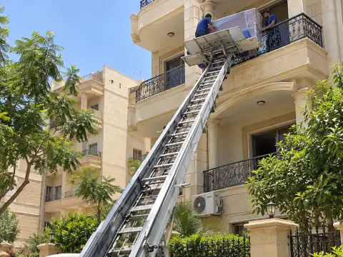 ونش يرفع قطعة أثاث مغلفة إلى شرفة مبنى سكني